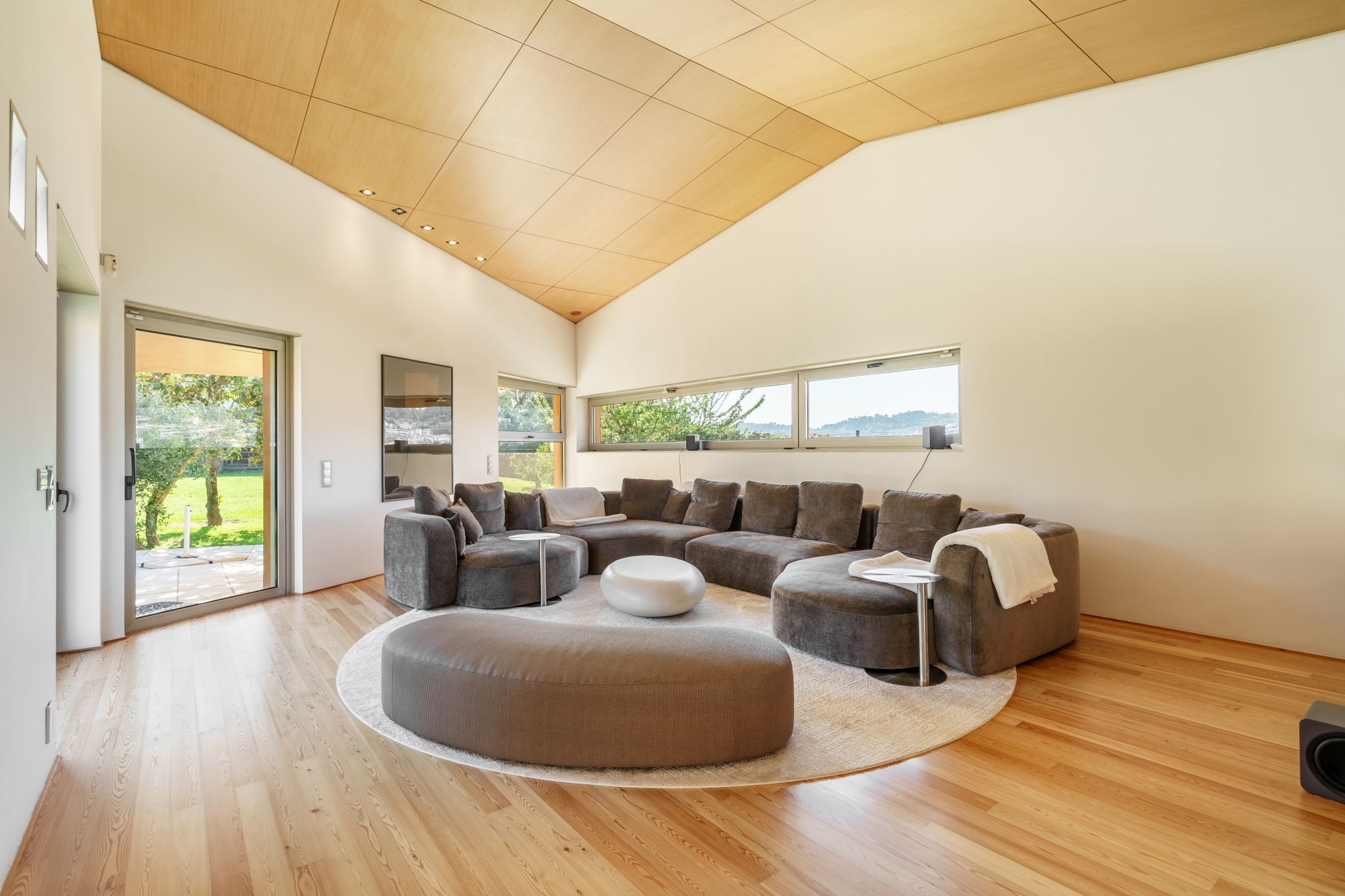The living room of Matos Essence Villa — vaulted wood ceiling, light pine floor, garden beyond.