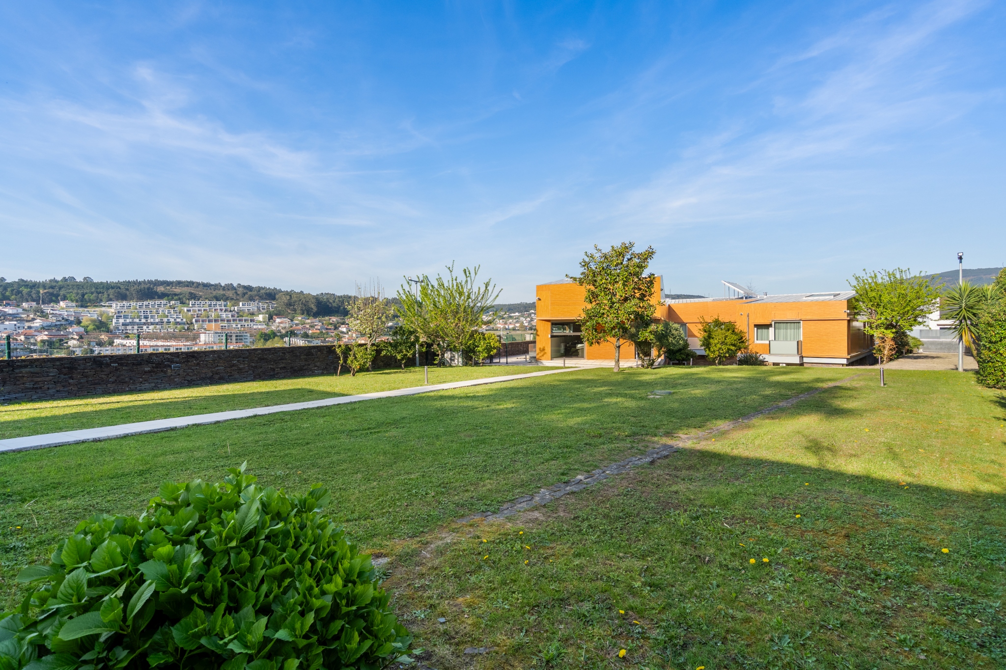 The villa from across the lawn — orange wood-clad façade, hills of Braga in the distance.
